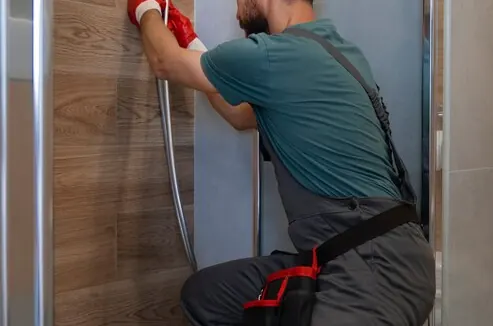 Instalator îngenuncheat în cabina de duș, lângă țeava de scurgere